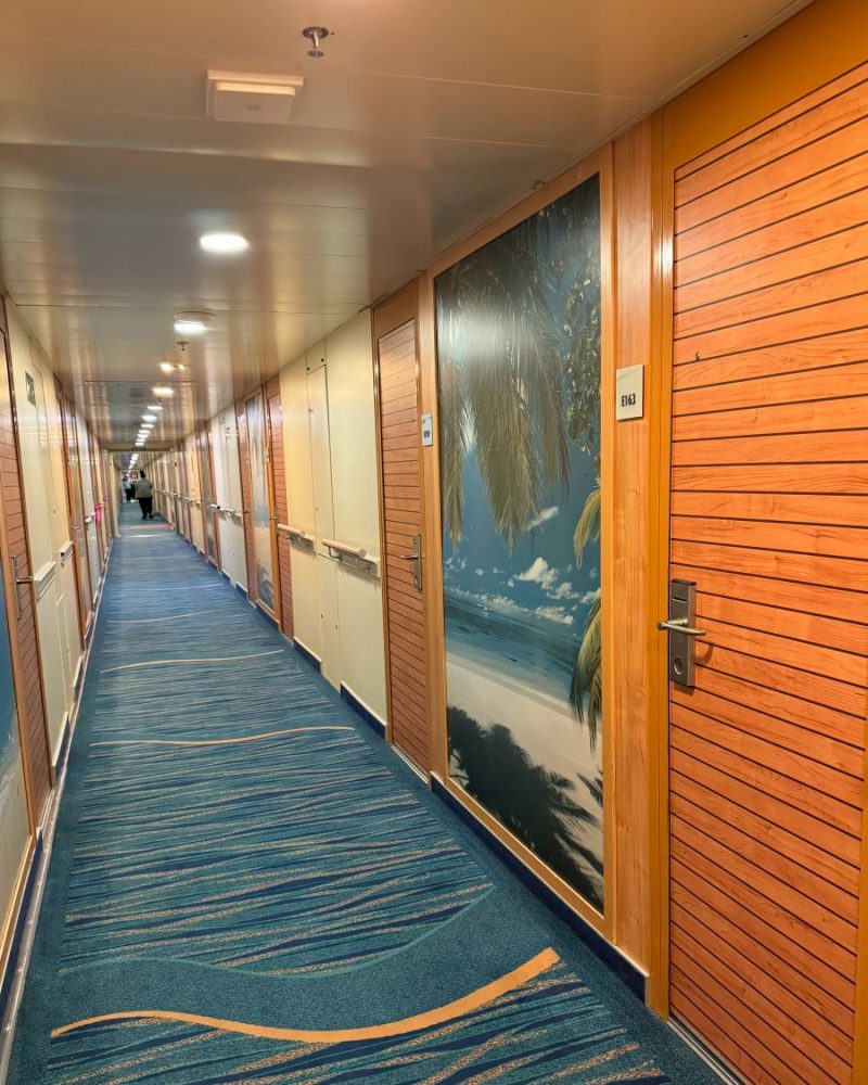 Carnival Elation review shows cabin hall with new carpet, tropical murals and woodgrain doors with keycard locks.