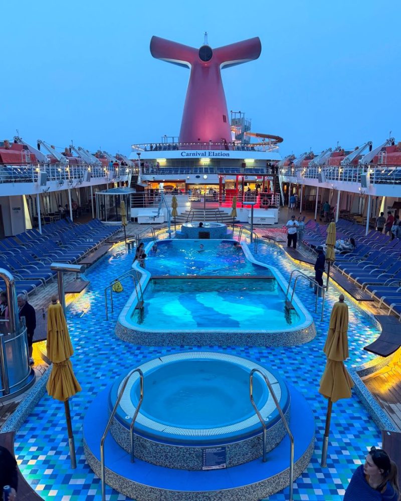 Pool Deck on the Carnival Elation at dusk with sun decks, lifeboats and ship's tail showing.
