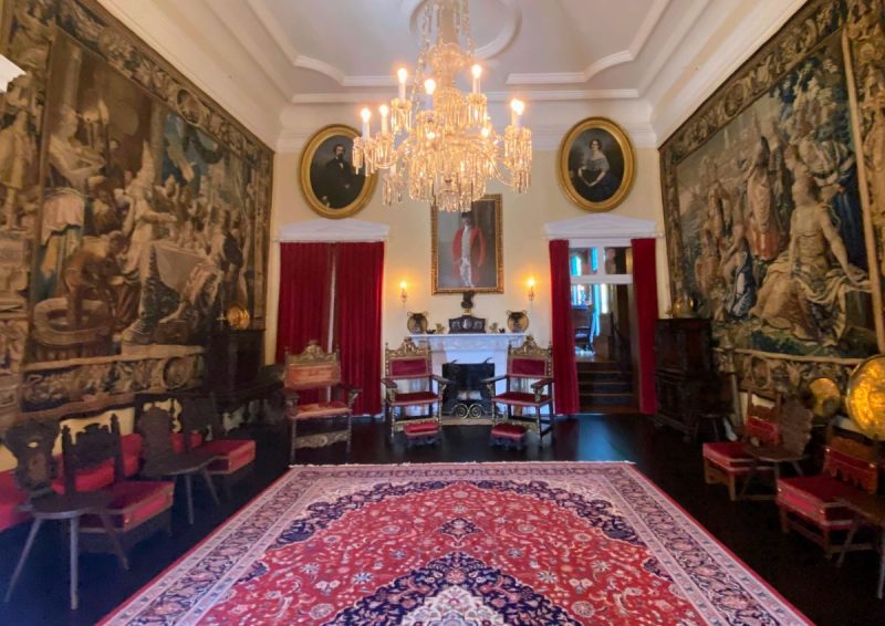 Formal room at the Davis Mansion, with tapestries on the wall, a massive crystal chandelier, red satin covered furniture and Oriental rug.