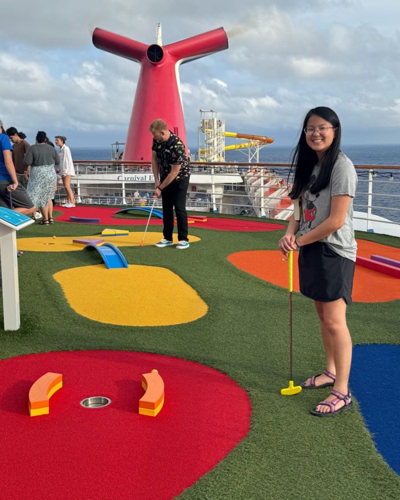 Putt Putt Golf on Deck 14 of Carnival Elation with girl smiling and cruise director taking his shot.