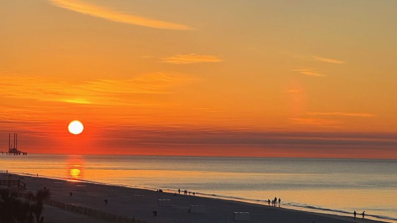 Sunrise on the beach in Gulf Shores, Alabama with silhouettes of people walking along the shore.