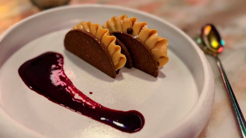 Chocolate tacos with fruit sauce on white plate.
