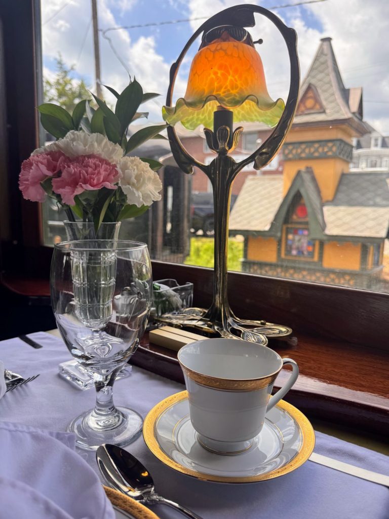 Table setting with brass lamp, flowers and fine china at Colebrookdale Railroad with depot in background.
