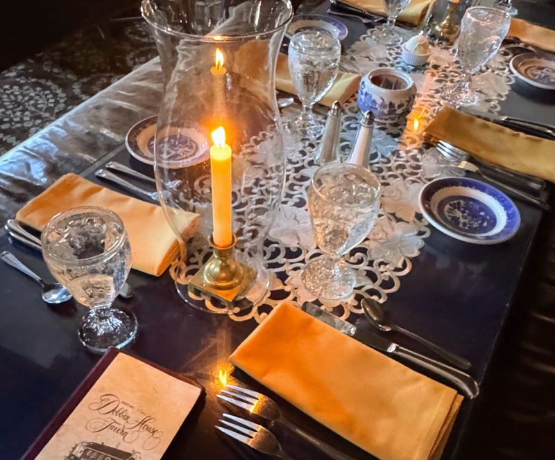Table setting at Dobbin House Dining Room with lace runner, yellow candle in sconce, blue china bread plates, silverwear and napkins.