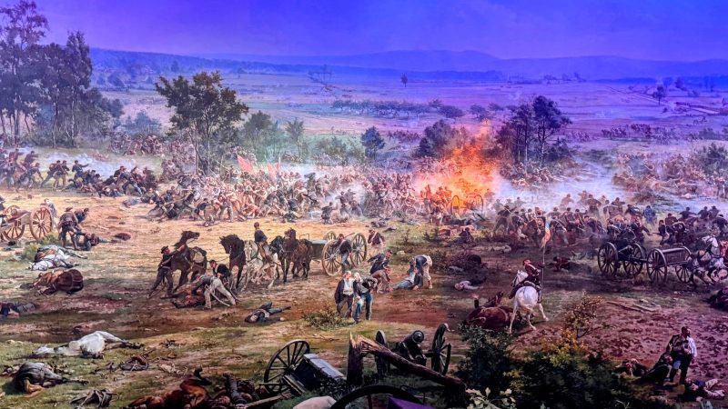 A portion of the Battle of Gettysburg as depicted on the Gettysburg Cyclorama, showing horses, downed soldiers and cannon fire in a field.