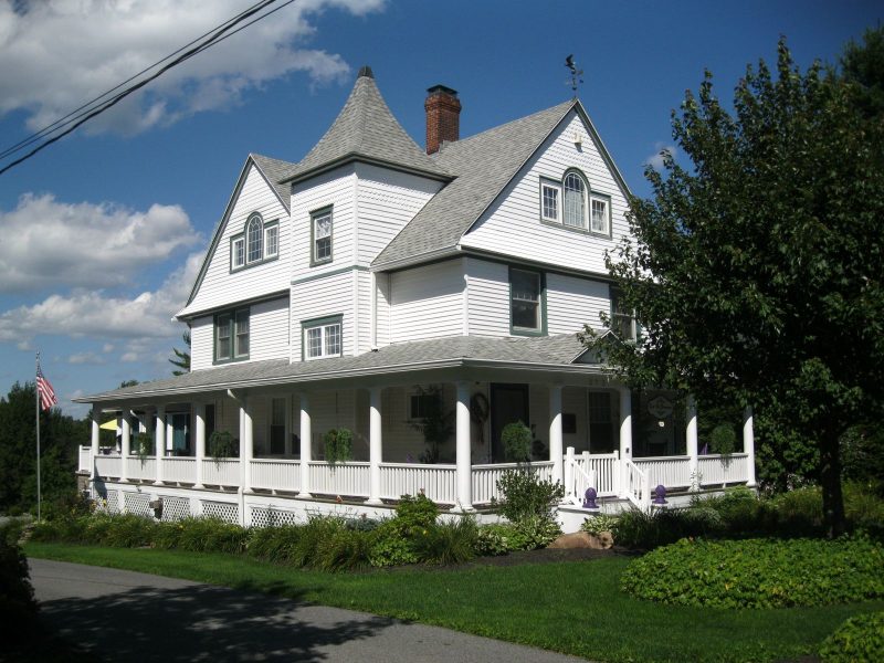 White house with wraparound porch and green trim indicative of cottage architecture.