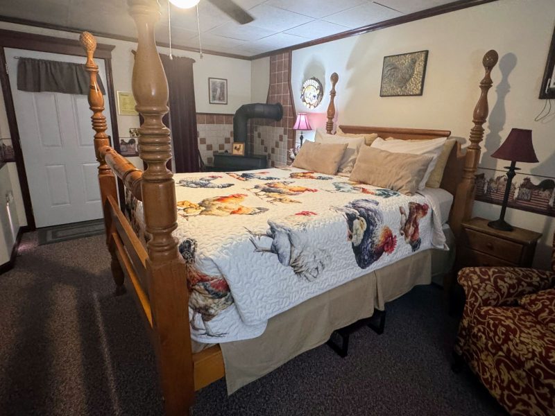 Guest room at Sleepy Hollow Inn B&B with queen size bed in rooster print coverlet, wood burning stove and sitting area.