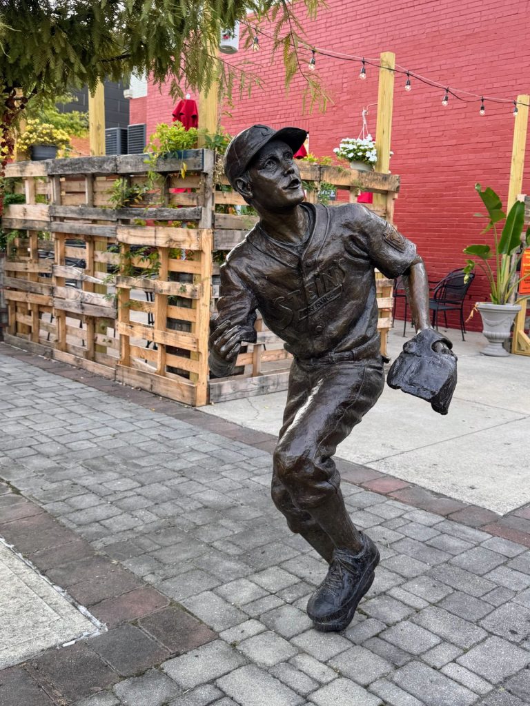 Statue of young boy in baseball uniform with glove looking up for the ball.