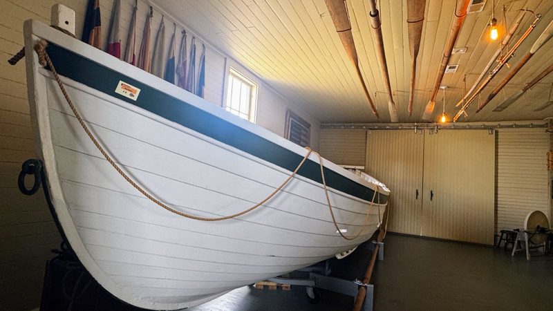 Life saving boat used in rescues with signal flags behind and oars hanging from the ceiling.